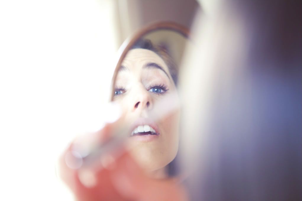 bride applying mascara through mirror